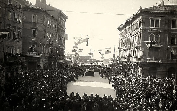 Celebration of a religious service in a road of Fiume, at the presence of military troops and the population, who throngs the road, decorated with buntings. The image was taken during the city occupation of Fiume by part of the Italian legionary troops, headed by Gabriele D'Annunzio