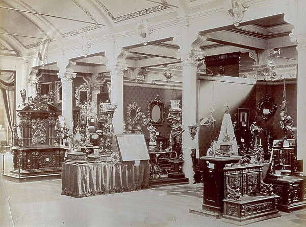 Exhibition room in the National Exposition of Milan of 1881. Cabinet furniture (clearly visible a large bench and an altar), statuettes in bronze and mirrors by the firm Besarel of Venice. The room in which the exhibit is installed is covered by a vault on piers. Coats of arms are set at the springing of the vaults