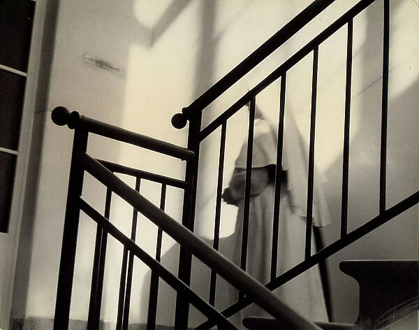 Internal staircase of a building from which a nun wearing a white clothe is coming down