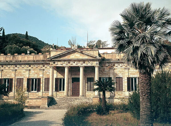 Main facade of Napoleon's Villa of San Marino in Portoferraio, on the island of Elba. The entrance is characterized by a porch with a gable on four columns. In the foreground a palm tree in the garden in front