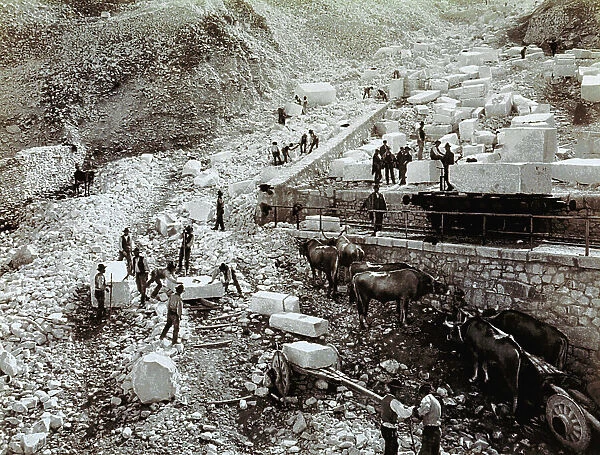 Railway station with laborers loading marble blocks onto railway wagons, three pairs of oxen with transport wagons are visible