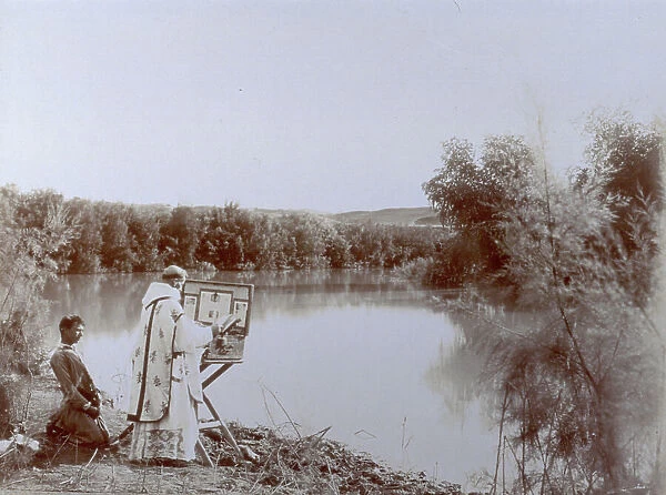 A stretch of the river Jordan in Israel, the banks densely covered with trees. On the banks, in the foreground, a priest and a young man praying