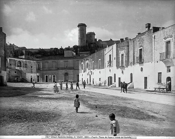 View of the Castle from a square of the town in Oria, province of Brindisi. Some kids playing, passersby and a local man with horse are visible