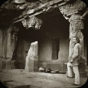 A bearded man stands in front of 3 ornately carved columns