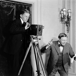 Two men making a film using a movie camera indoors in Americ