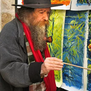 A street artist, with a long beard smoking a large pipe