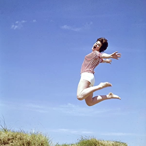 Young woman leaps up from a sand dune