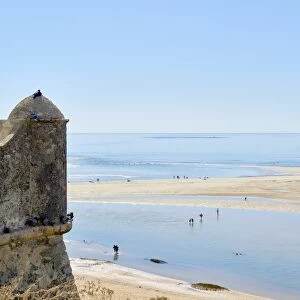 Beachgoers crossing a lagoon formed by the low tide, and detail of a watchtower in Cacela Velha