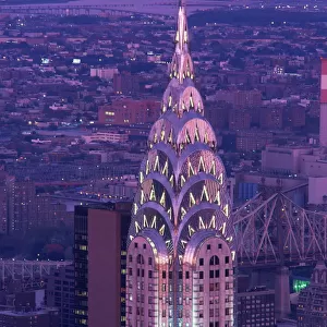 The top of the Chrysler Building illuminated in the evening with a bridge