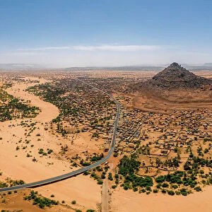 A crumbling mountain, a river bed, palms, and dunes surround the village of Kamour, Mauritania, Sahara Desert, West Africa, Africa