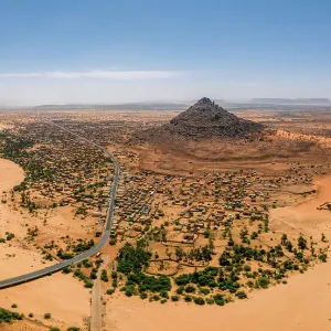 A crumbling mountain, a river bed, palms, and dunes surround the village of Kamour, Mauritania, Sahara Desert, West Africa, Africa