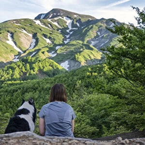 A girl sitting beside her border collie dog staring at a mountain landscape of Cusna Mountain, Emilia Romagna, Italy, Europe