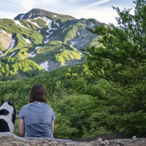 A girl sitting beside her border collie dog staring at a mountain landscape of Cusna Mountain, Emilia Romagna, Italy, Europe