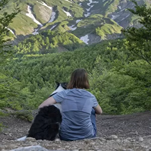 A girl sitting beside and hugging her border collie dog staring at a mountain landscape of Cusna Mountain, Emilia Romagna, Italy, Europe