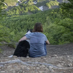 A girl sitting beside and hugging her border collie dog staring at a mountain landscape of Cusna Mountain, Emilia Romagna, Italy, Europe