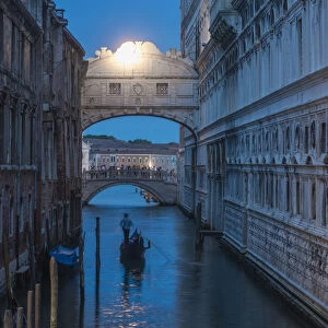 Gondolas pass under the Bridge of Sighs beside the Doges Palace in Venice at twilight