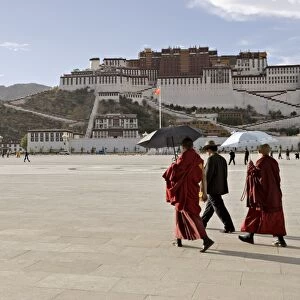 Monks carrying umbrellas to shield against the sun, in front of the Potala Palace