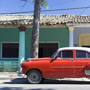 Red vintage American car parked on street next to colourful buildings in Vinales
