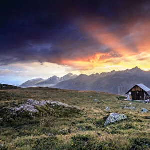 Wooden hut under fiery sky and clouds at sunset, Muottas Muragl, St. Moritz, Canton of Graubunden