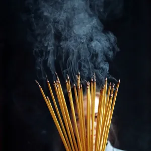 Young Chinese woman praying with big burning incense sticks in her hands