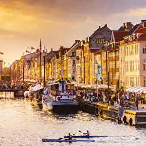 Two people kayaking in the Nyhavn canal in Copenhagen at sunset, Denmark