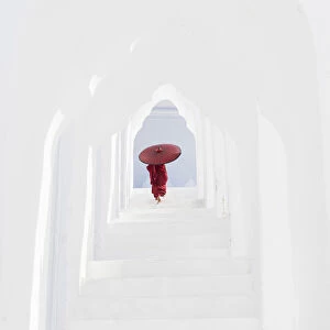 A young Buddhist monk holding a red umbrella walks up the steps in Hsinbyume Pagoda