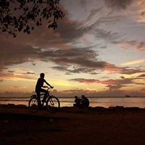 A boy rides a bicycle along a promenade in the evening in the southern Indian city