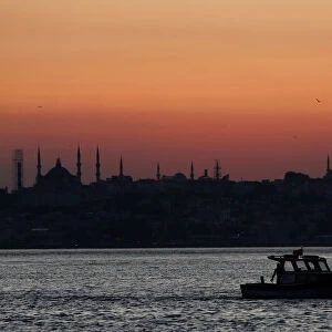 A fishing boat sails in the Bosphorus as the sun sets over the old city in Istanbul