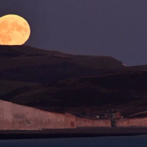 The moon is seen rising behind the Seven Sisters Cliffs at Birling Gap in East Sussex