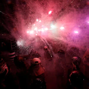 Participators wearing motorcycle helmets get sprayed with firecrackers