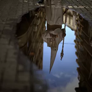 A penitent is reflected in a puddle of water after rain fell at the Humildad