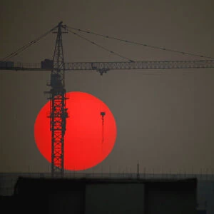 The sun sets behind a crane behind a construction site for a new residential building in