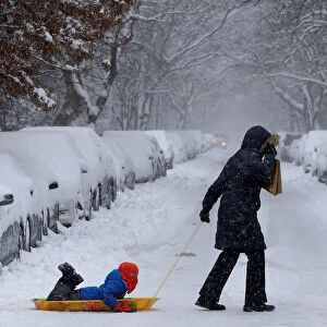 A woman pulls her child on a sled in heavy snow in Brooklyn, New York City