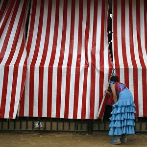 A woman wearing a traditional Sevillana dress looks into a stall at a fair in Seville