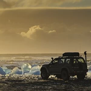 Nissan Patrol 4x4 tour guide vehicle at edge of glacial ice in lake at dusk, Jokulsarlon Lagoon, Vatnajokull Glacier