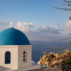 Blue domed Greek Orthodox church with bougainvillea flowers in Oia, Santorini, Greece