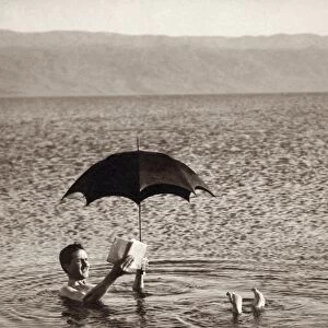 HOLY LAND: DEAD SEA. A man floating in the Dead Sea with an umbrella and a book
