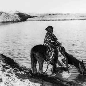 NAVAJO & HORSE, c1915. A Navajo Native American seated on a horse that is drinking from a lake or river in the southwestern United States. Photograph, c1915