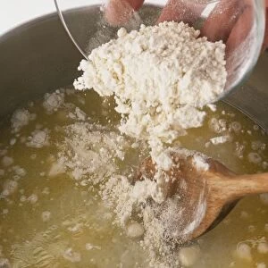 Adding flour to melted butter and stirring with a wooden spoon until combined (making choux pastry), close-up