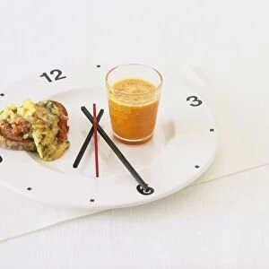 Carrot juice and toasted rye bread with herbed scrambled egg, on a plate with a clock face on it