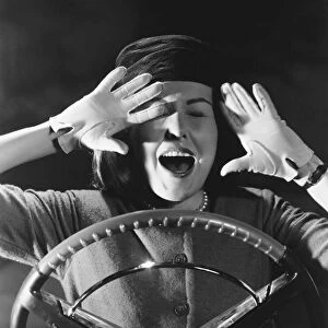 Frightened lady sitting behind steering wheel of car, black and white