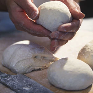 Hand shaping dough into ball, fresh dough, dough balls and pizza peel on kitchen surface