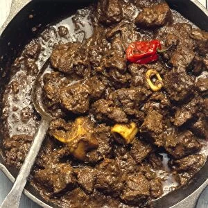 Jamaican goat curry, mixed with cut up bones and chillies in thick brown sauce, in frying pan
