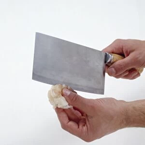 Man rolling blade of meat cleaver along back of raw prawn to make shallow cut