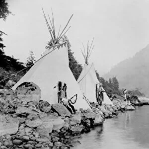 Three Native American men, probably Umatilla, stand on shore of river next to tepees