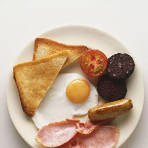 Plate of full English breakfast, fried egg, slices of bacon, sausage, toast, fried tomato and black pudding