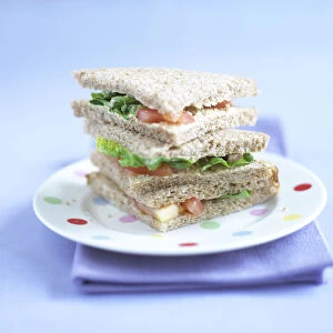 Three triangular sandwiches piled up on dotted plate, purple napkin underneath
