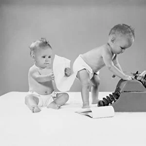 Baby standing at typewriter, twin seated behind looking at papers