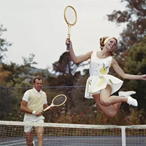 Couple on tennis court, woman jumping in foreground