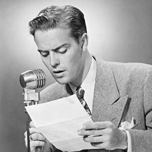Elegant man talking into microphone in studio, (B&W)
